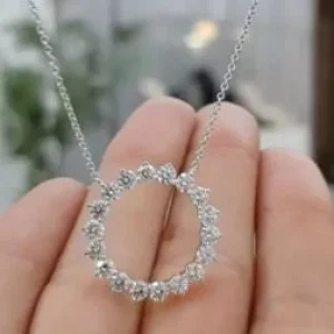 A brilliant silver or white gold necklace featuring an open-circle pendant set with large, shimmering round-cut stones. The pendant is shown suspended from a thin link chain and held in front of a hand to showcase its scale and sparkle.