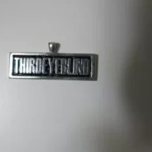Rectangular silver pendant featuring the raised text "THIRDEYEBLIND" against a black recessed background.
