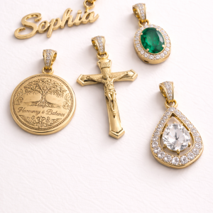A collection of five premium gold pendants displayed on a white textured surface. The set includes a "Sophia" cursive nameplate, an oval emerald green stone with a diamond halo, a detailed crucifix, a "Harmony & Balance" tree of life medallion, and a pear-shaped pendant featuring a large clear center stone surrounded by a shimmering halo. All pieces feature iced-out bails for added brilliance.