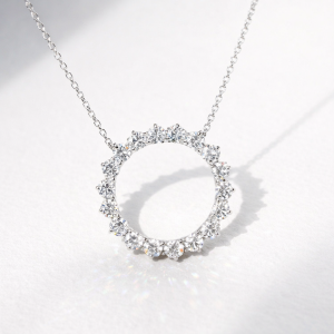 A brilliant silver or white gold necklace featuring an open-circle pendant set with large, shimmering round-cut stones. The pendant is shown suspended from a thin link chain and held in front of a hand to showcase its scale and sparkle.